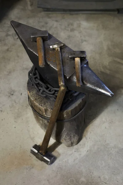 Above view of various hammers for forging place on steel anvil, big sledgehammer leaning on anvil in workshop