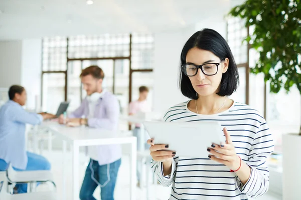 現代の部屋に立って タブレット上のオンラインソースを分析する眼鏡で深刻なペンシブ若い女性フリーランサー — ストック写真