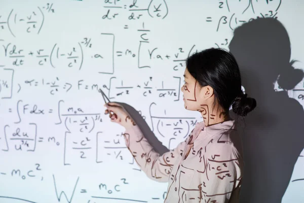 Confident Asian math student with hair bun standing against projection screen and giving presentation