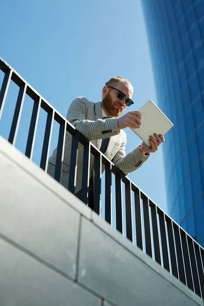난간에 기대어 태블릿에 데이터를 선글라스에 심각한 사업가의 아래보기 — 스톡 사진