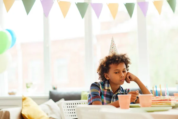 Portrait of sad African-American boy sitting alone at Birthday party, copy space