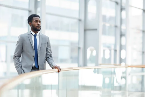 Serious purposeful young black business owner of large corporation standing by railing in modern office and being deep in thoughts