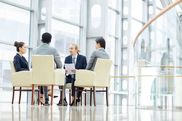 Group of experienced business experts in formalwear sitting in circle and discussing sales data together