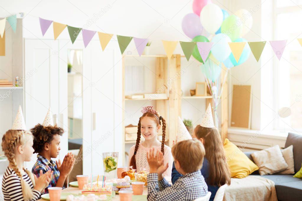 Portrait of happy red haired girl celebrating birthday  party sitting at table with friends, copy space
