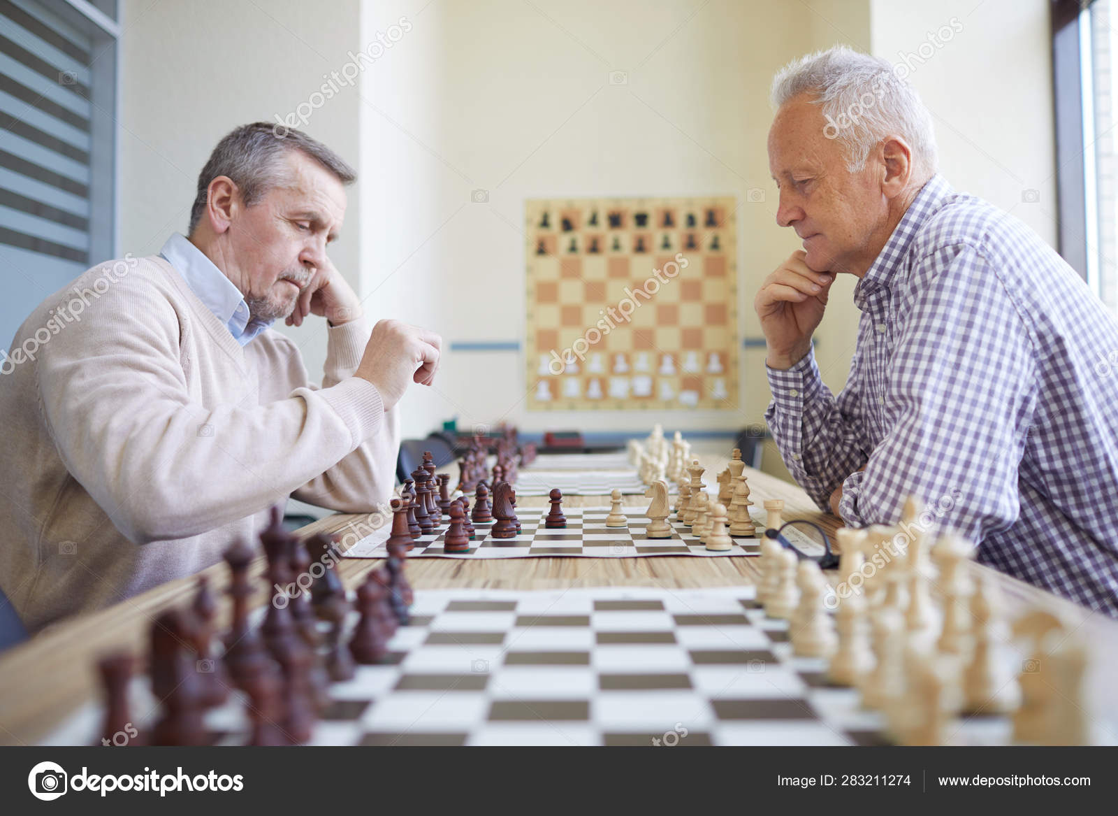 Old man in checked shirt holding glasses and thinking about next chess move  in game with imaginary opponent Stock Photo