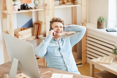 Rahat gömlek içinde gülümseyen pensive yakışıklı genç yönetici sandalyede rahat poz oturan ve cep telefonu konuşurken başını kaşıma