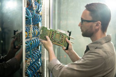Ciddi konsantre genç sakallı sunucu onarım profesyonel gözlük sunucu rafları kabine ayakta ve raf donanım yükleme