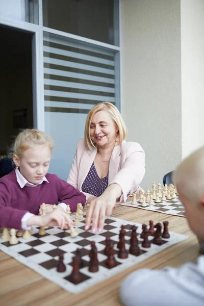 Uśmiechnięta Kobieta Nauczyciel Pomaga Dzieciom Nauczyć Się Grać Szachy Wyjaśnić — Zdjęcie stockowe