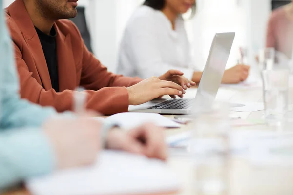 Closeup of business people sitting in row at meeting table, focus on Middle-eastern man using laptop, copy space