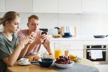 Mutfakta servis edilen masada otururken sosyal ağlarda arama yapan genç çağdaş çift
