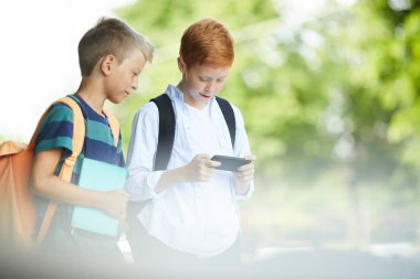 İki sınıf arkadaşı sıcak bahar sabahı okula giderken açık havada telefonla oynuyor