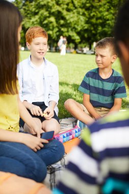 Okuldan sonra parkta çimenlerin üzerinde oturan, konuşan ve notlarını tartışan dört öğrenci