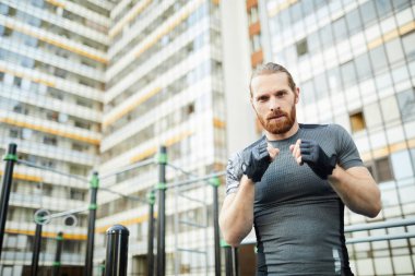 Kırmızı sakallı kendine güvenen yakışıklı genç adam spor sahasında tek başına kickboks pratik parmaksız eldiven giyiyor