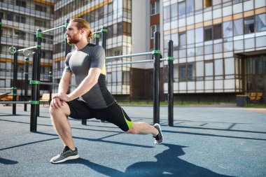 Açık havada statik egzersiz yaparken diz ve germe bacaklar ellerini yaslanmış sıkı spor giyim genç kırmızı sakallı adam