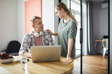 Genç kadın elini kocasının omzunda tutarken ikisi de masaya birbirlerine bakıyor.