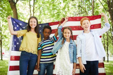 Bağımsızlık gününü kutlarken ormanda duran ve Amerikan bayrağını bir arada tutan rahat kıyafetler giyen çok ırklı bir grup olumlu çocuk