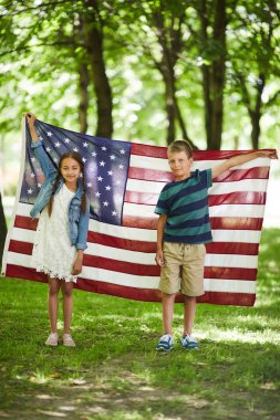 Ormanda ayakta ve ulusal bayrak tutan rahat kıyafetler içinde gülümseyen dostu Amerikalı çocukların Portresi