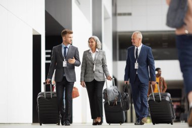 Tekerlekli bavulları taşıyan ve havaalanını birlikte geçen formalwear forum katılımcılarından oluşan kendinden emin ekip