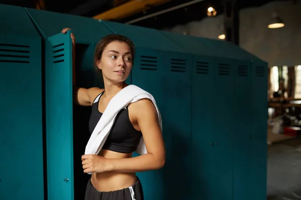 Dramatic waist up portrait of young woman standing by locker in sports club and looking away, copy space