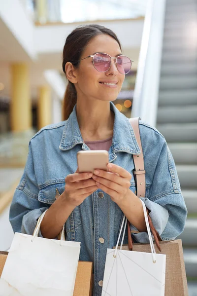 Young smiling texting on phone arranging meeting with friend in mall after successful shopping