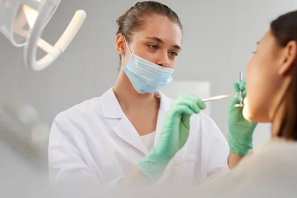 Retrato Jovem Dentista Usando Máscara Facial Enquanto Examina Paciente Clínica — Fotografia de Stock