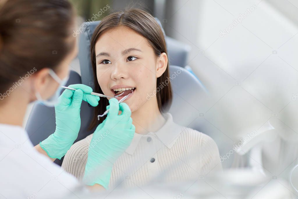 High angle portrait of smiling Asian girl sitting in dental chair during check up, copy space