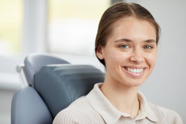 Diş sandalyede otururken kamera gülümseyen ve mükemmel beyaz dişleri gösteren güzel genç kadının baş ve omuzportresi, kopya alanı