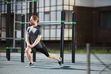 Fit yakışıklı genç sakallı adam at kuyruğu çömelme ve açık havada germe egzersiz icra ederken düz ellerini yükselterek