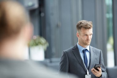 Konferans lobisinde duran ve akıllı telefon kullanarak rozeti ile Ciddi düşünceli yakışıklı temsilcisi