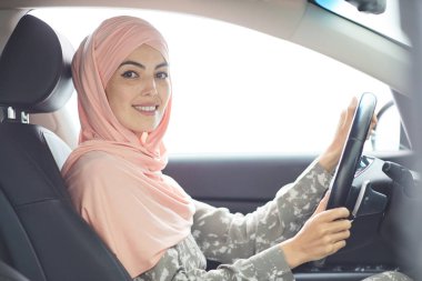 Pembe hijab direksiyon önünde oturan neşeli çekici genç Müslüman bayan sürücü portresi