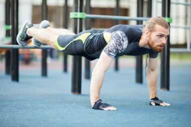 Konsantre kararlı genç kırmızı sakallı adam spor giyim açık havada eğitim için spor zemin ekipmanları kullanarak