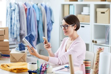 Casualwear internet mağazası yöneticisi masa başında otururken akıllı telefon yeni denim çapraz ayakkabı fotoğraf çekmek