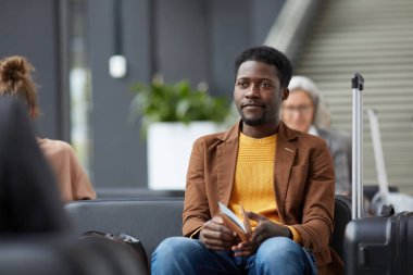 İçerik Sakallı Afro-Amerikan adam havaalanı bekleme alanında oturan ve pasaport ve biniş kartı tutan