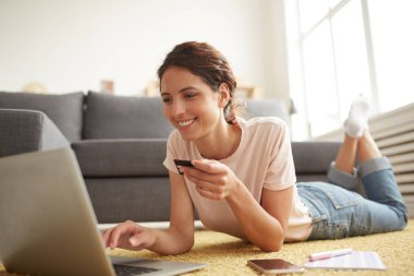 Rahat giyim neşeli güzel genç bayan yerde rahat poz yalan ve kredi kartı ile online ödeme yaparken dizüstü bilgisayar kullanarak