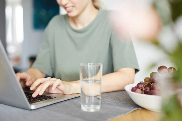 自宅の台所のテーブルのそばに座って ネットワーク中にラップトップのキーパッドに入力する若い女性 — ストック写真
