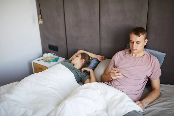 ベッドに座っている間 彼女のスマートフォンで妻のメッセージを読んで若い不審な男 — ストック写真