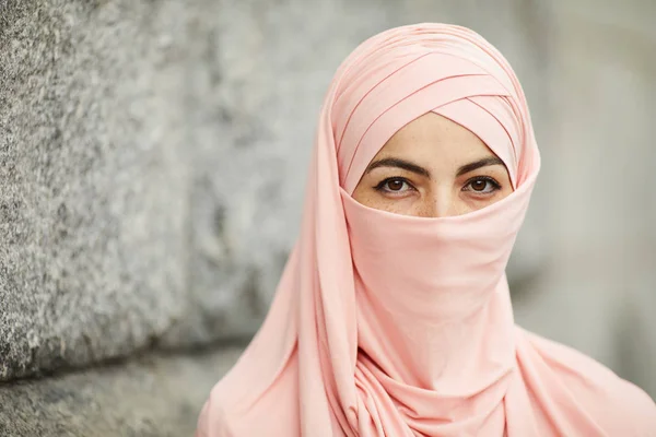 身穿粉色头巾 长着棕色眼睛的美丽雀斑的穆斯林妇女站在石墙旁边的画像 — 图库照片