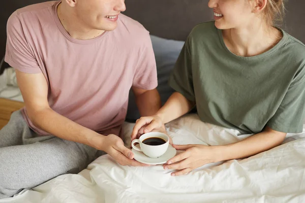 コーヒーを飲みながらベッドに座りながら お互いを見つめ合う笑顔の若い男女 — ストック写真