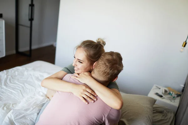 朝ベッドに座っている間 夫を抱きしめる陽気な若い女性 — ストック写真