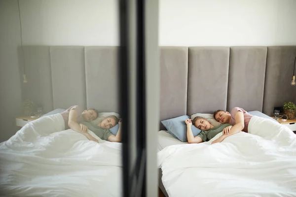 ワードローブのドアの鏡で毛布の下にベッドに横たわっている若い愛情の睡眠カップル — ストック写真