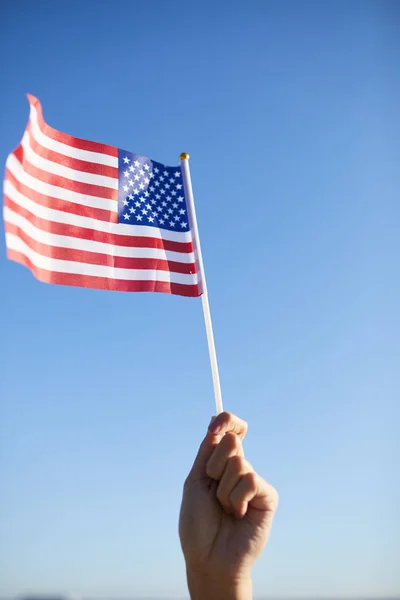 Close-up of unrecognizable person raising hand with American flag on stick in air while celebrating independence day