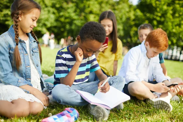 Two Teenage Friends Doing Homework Sitting Grass While Classmates Playing — Stock Photo, Image