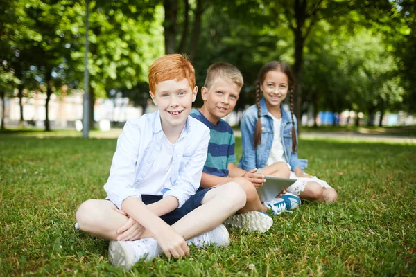 Tre Leende Skolbarn Parken Sitter Gräs Roligt Tillsammans Sommarlovet — Stockfoto