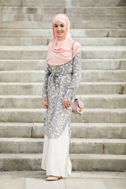 Yaz hijab ve uzun elbise merdivenlerde karşı duran omuz küçük çanta giyen ve kameraya bakarak gülümseyen şık genç Müslüman kadın
