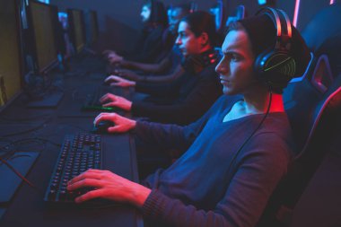 Ciddi konsantre esports oyuncu masada oturan kablolu kulaklık giyen ve online multiplayer oyun oynamaya oyun konsantre
