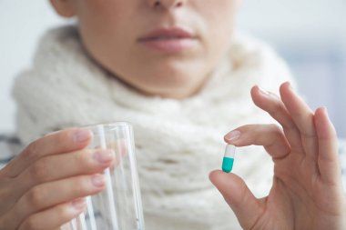 Boynunda sıcak atkı ile genç kadının yakın çekim su bardağı tutan ve antiviral alarak