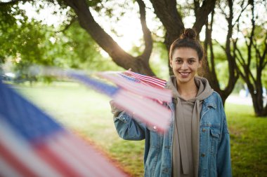 Amerikan bayrağı çelenk ile süslenmiş parkta duran saç topuz ile gülümseyen hipster kadın Portresi