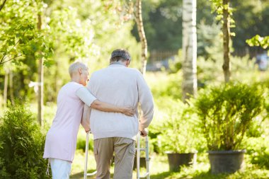 Hemşire veya eşi ile parkta yürüyen yürüteç eğilen kıdemli adam arka görünüm portresi, kopya alanı