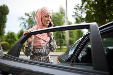 Arabaya binerken telefonda konuşurken geleneksel elbiseli Pretty genç Müslüman kadın