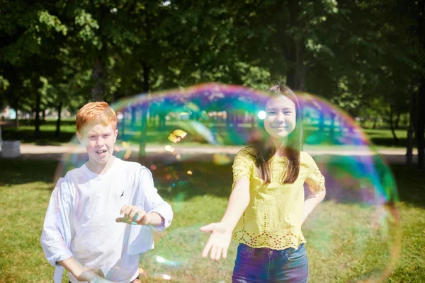 夏の公園で石鹸の泡をキャッチ遊び心のある子供たち 混乱した顔を持つ赤毛の少年がバブルに手を伸ばす — ストック写真